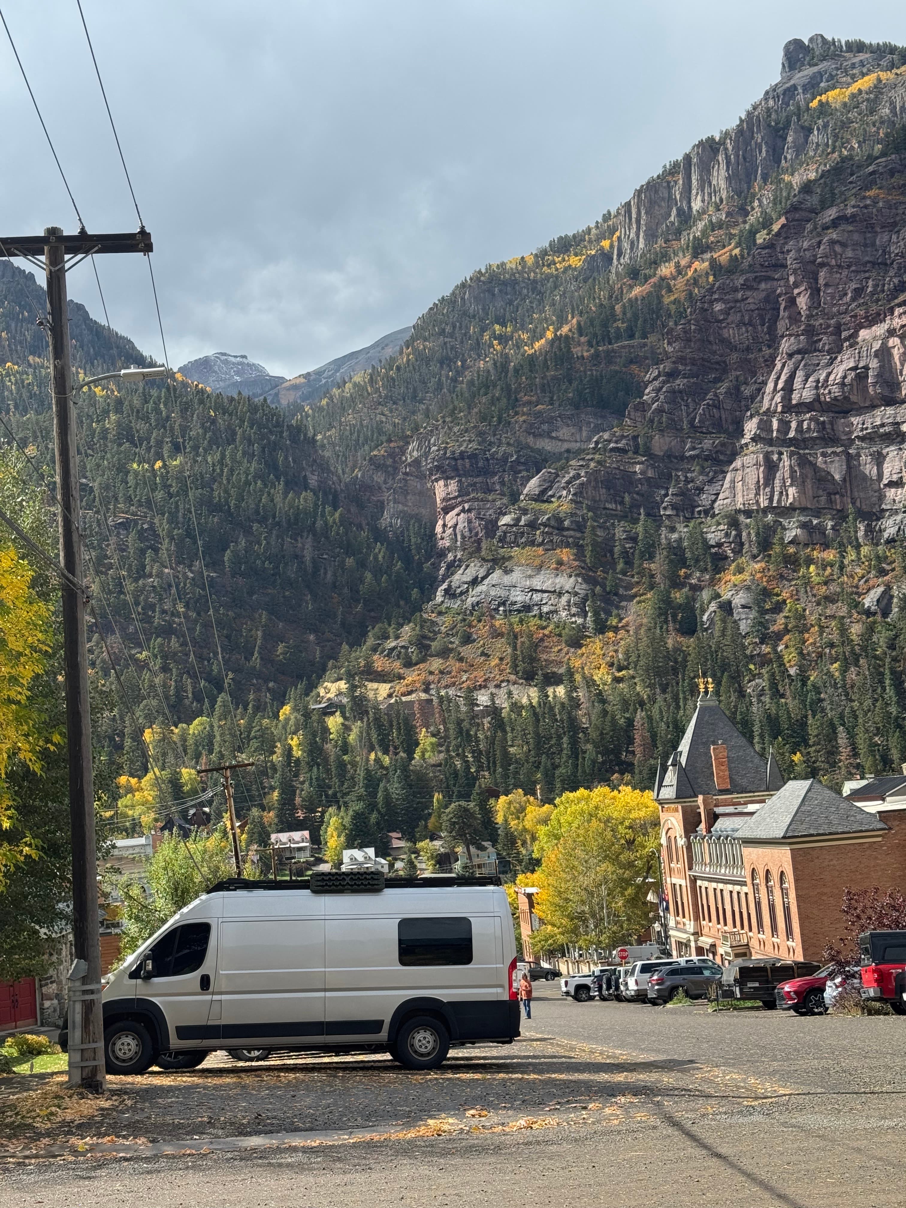 The Upward Buzz campervan parked on a gravel street in Ouray, Colorado, surrounded by dramatic Rocky Mountain cliffs and autumn foliage